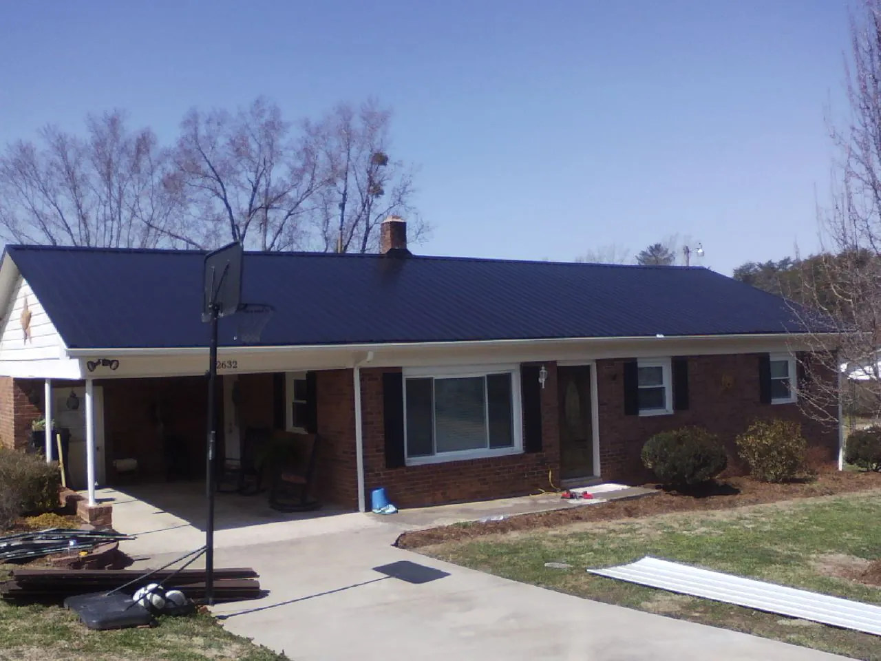 Finished dark blue metal roof on a brick ranch with a carport in Plainview