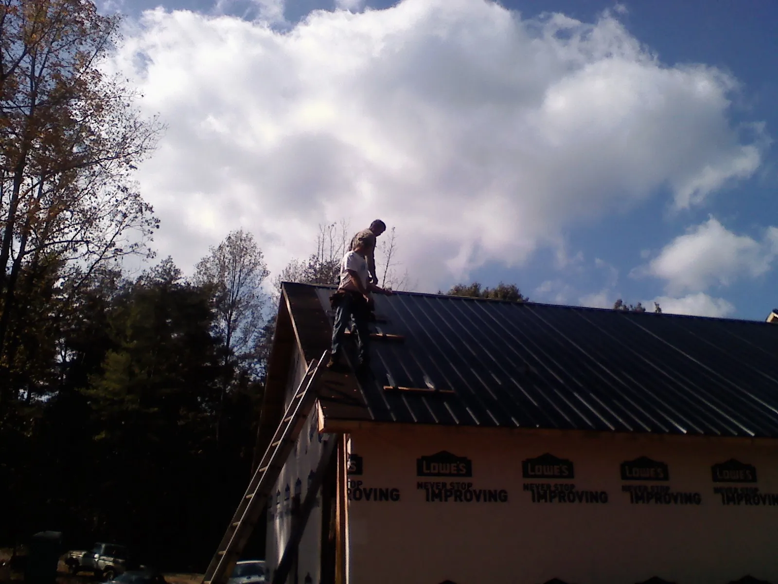 Roofer fastening dark metal panels high against a cloudy sky, from a Roof Inspection job in Plainview